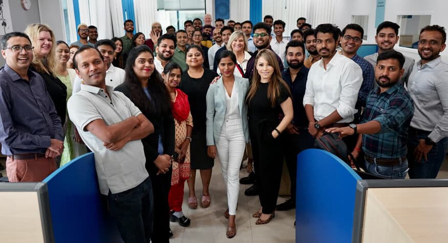 Large team of diverse office professionals posing together in a bright, modern open-plan workspace.