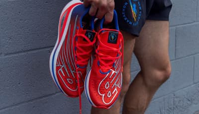 A person holding a pair of red and blue New Balance FuelCell running shoes with New York City Marathon branding.