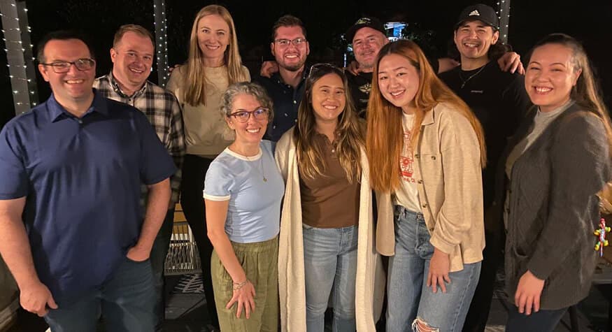 Diverse team members smiling for a group photo during an evening company social event.