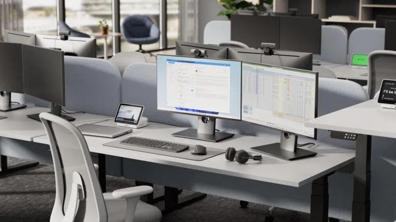 Modern open-office layout featuring dual-monitor workstations with Logitech webcams and headsets.