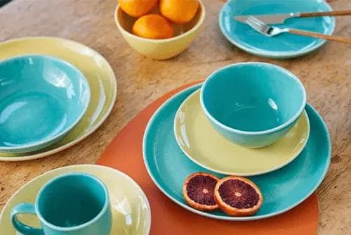 Briscoes vibrant teal and yellow ceramic dinnerware set with bowls, plates, and a mug on a wooden table.