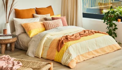 A bed styled with warm-toned linens in shades of yellow, orange, and terracotta, featuring various textured decorative pillows.