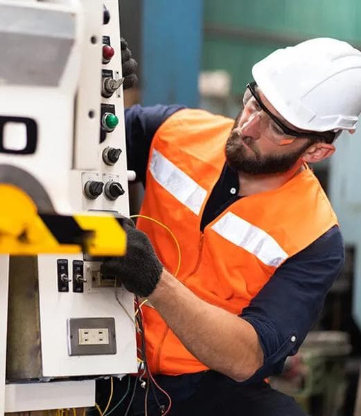 Adobe Stock - Electrician in a hard hat and orange safety vest working on an industrial control panel with colored wires.