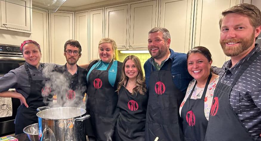 Coworkers participating in a team-building cooking class together in a professional kitchen.