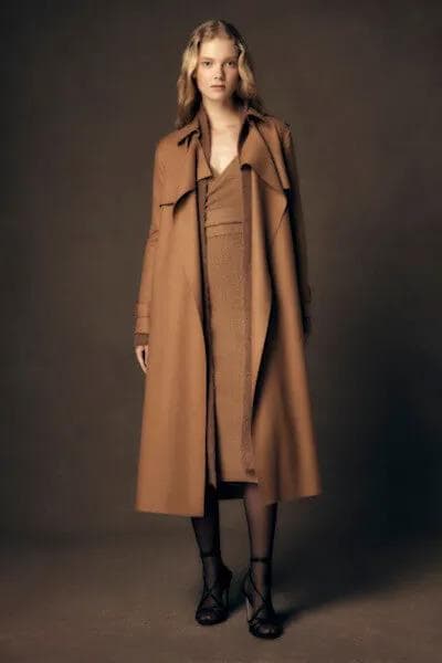 Woman walking - Model wearing a long camel brown trench coat over a matching knit dress and strappy black heels.