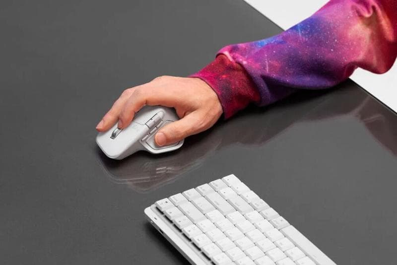 Person using a white Logitech ergonomic mouse and mechanical keyboard on a dark desk.