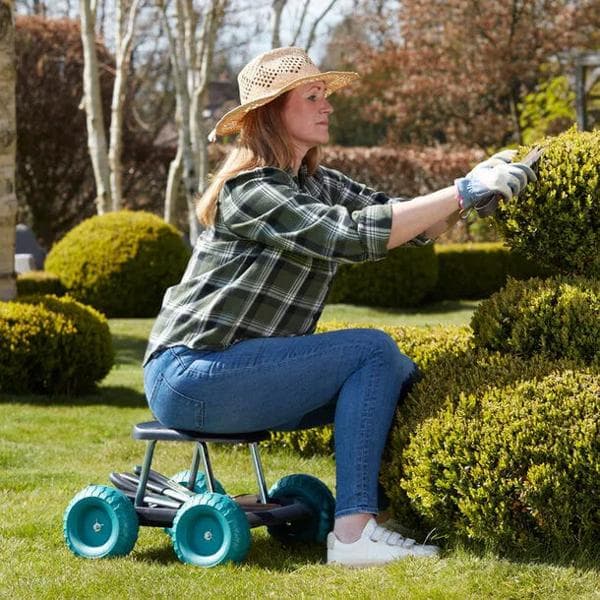 Easylife product imagen- Woman using a rolling garden stool with teal wheels to prune hedges with hand shears.