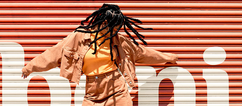 Woman in orange clothes dancing in front of orange wall with Beni painted on it